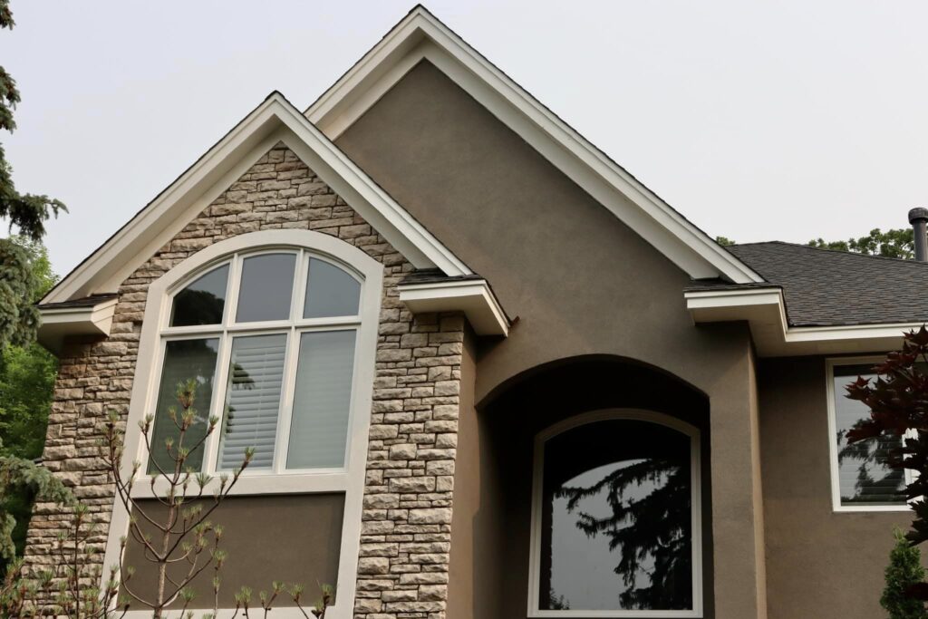 A modern house exterior with stone and stucco siding, a large arched window, and a pointed roofline, surrounded by trees—expertly maintained by an exterior contractor Minnesota for seamless stucco repair and lasting beauty.