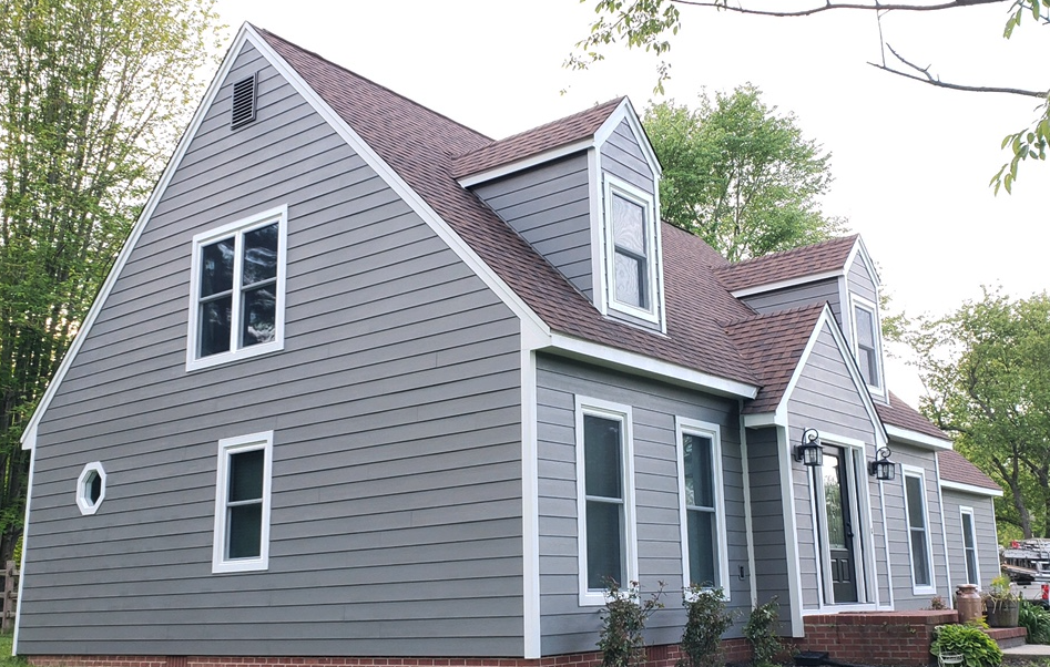 A modern gray house with white trim, multiple gables, and large windows stands amid green trees—expertly maintained by a trusted stucco contractor Twin Cities to ensure lasting beauty.