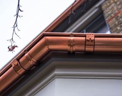 Close-up of a copper rain gutter system installed along the edge of a house roof by an exterior contractor in Minnesota, with part of a branch visible in the background.