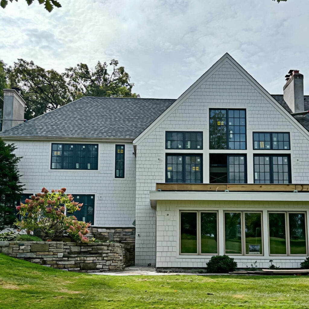 A modern two-story white house with large black-framed windows, a partially covered balcony, stone landscaping, and a well-kept lawn—expertly finished by an exterior contractor Minnesota homeowners trust.