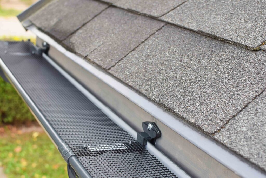 A close-up view of a house roof with asphalt shingles and a black metal gutter guard installed along the edge by an exterior contractor Minnesota.