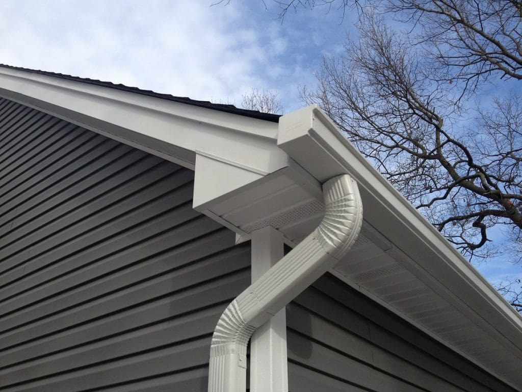 Close-up of a house corner showing vinyl siding, a white rain gutter system, and leafless tree branches in the background under a partly cloudy sky—perfect inspiration for those seeking an exterior contractor Minnesota homeowners trust.