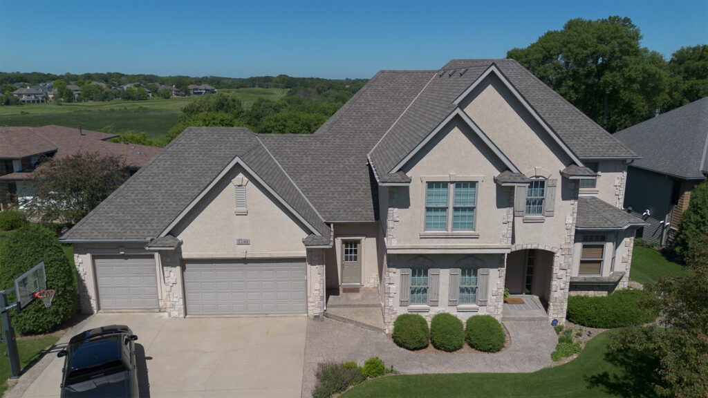 Two-story suburban house with a three-car garage, stone and stucco exterior, front lawn, and a driveway, photographed on a clear day.